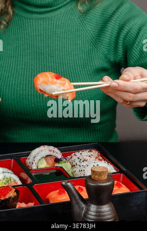 Ragazza in maglione verde che tiene il nigiri dalla scatola bento con le bacchette Foto Stock