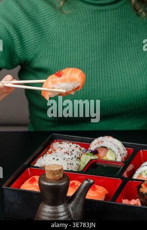 Ragazza in maglione verde che tiene il nigiri dalla scatola bento con le bacchette Foto Stock