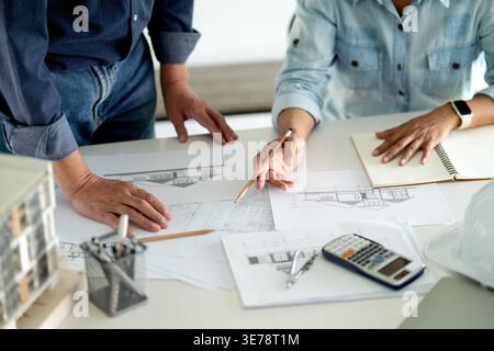 Architetti e ingegneri Un uomo e una donna sono seduti e seduti a guardare i progetti su un tavolo per discutere e discutere idee per la creazione di un costrutto Foto Stock