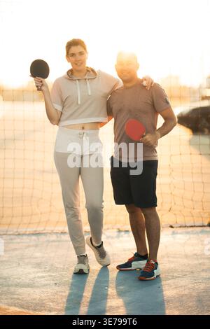 Coppia sorridente insieme con racchette da ping pong al tramonto Foto Stock