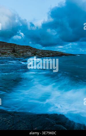 Le onde si infrangono sulla costa rocciosa della Svezia, mentre le nuvole si accumulano sopra la testa. La scena mostra la costa al crepuscolo con acqua che spruzza contro la terra. Foto Stock