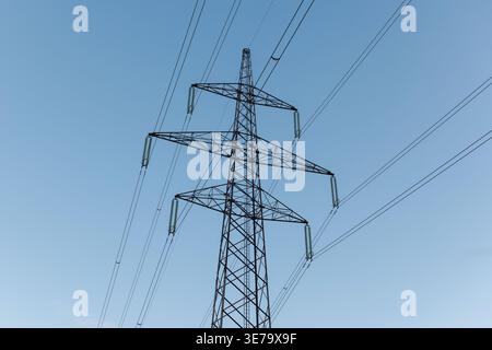 Le torri di trasmissione dell'energia elettrica si estendono lungo il paesaggio al tramonto, evidenziando il legame tra industria e ambiente. Foto Stock