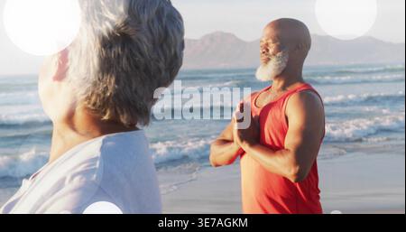 Meditare un uomo maturo che tiene una posa di preghiera sulla spiaggia sabbiosa, indossa la parte superiore senza maniche rossa, copia spazio Foto Stock