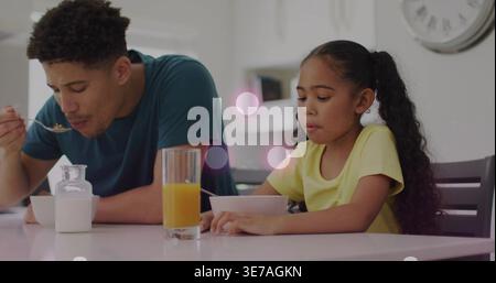 Mangiare il padre in camicia di tè, la figlia in camicia gialla al tavolo della cucina, con ciotole, cucchiai, succo di frutta Foto Stock
