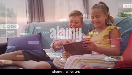 Fratelli preadolescenti seduti sul divano del soggiorno, tenendo il tablet e rispondendo alle bolle di notifica Foto Stock