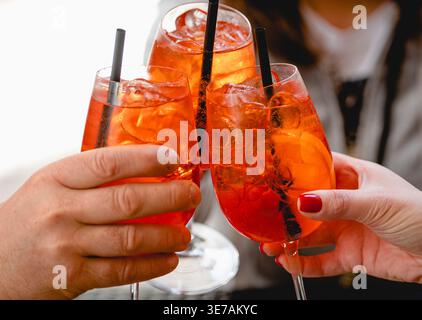 Gli amici brindano con cocktail Spritz all'arancia in bicchieri da vino, festeggiando insieme in un ambiente sociale Foto Stock