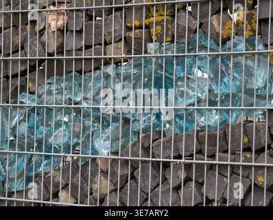 Una fotografia dettagliata e ravvicinata di una struttura decorativa a gabbia in gabbione, caratterizzata da strati di ciottoli di basalto grigio scuro e da una grande e vivace gl blu turchese Foto Stock