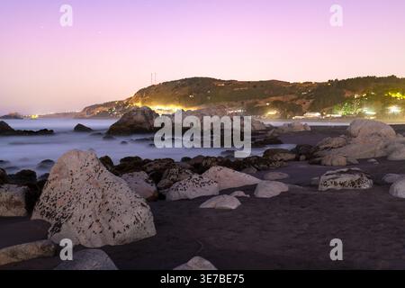 Grandi rocce granitiche e sabbia vulcanica scura definiscono la costa frastagliata del villaggio costiero di Matanzas in Cile. Foto Stock