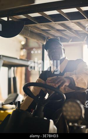 Uomo nero di mezza età che guida un carrello elevatore a forche in magazzino Foto Stock