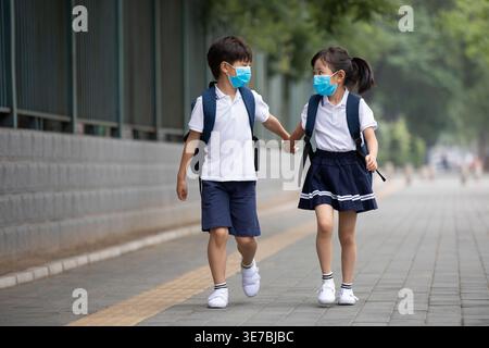 Alunni cinesi in uniforme scolastica che indossano maschere facciali che camminano per strada durante il giorno Foto Stock