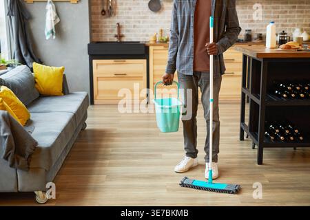 Uomo nero che tiene secchio e mocio camminando dopo la pulizia in cucina a casa Foto Stock