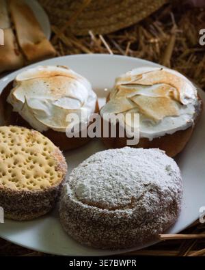 I dolcetti caldi da forno si trovano su un piatto rustico. Spiccano le consistenze di zucchero alla cannella, meringa e pasticceria friabile. L'illuminazione soffusa mette in risalto ogni singolo dessert Foto Stock