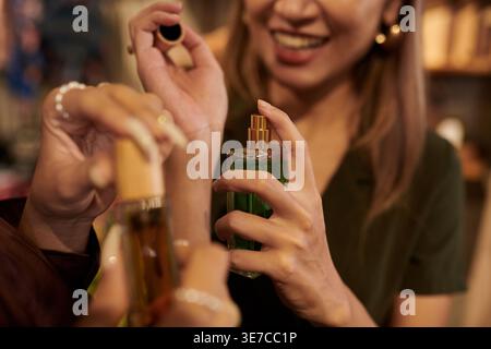 Donna asiatica che spruzza profumo al polso mentre si trova in una boutique Foto Stock