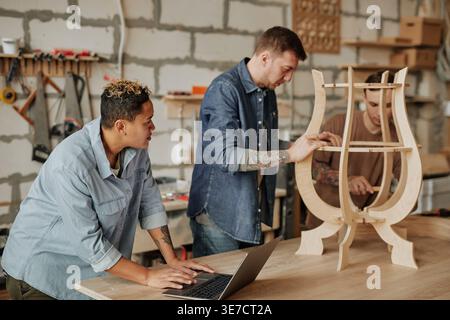 Gruppo diversificato di falegnami che lavorano con pezzi di legno sul tavolo in officina Foto Stock