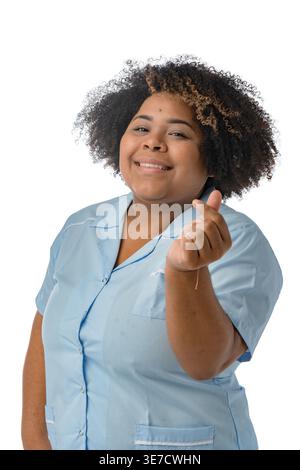Donna ispanica dalle dimensioni più grandi con afro riccio che indossa l'uniforme blu, che rende il cuore con le dita in piedi su sfondo bianco in studio Foto Stock