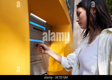 Donna giapponese in piedi per strada e ritirare soldi dal bancomat durante il giorno Foto Stock