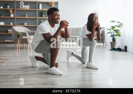 Allegra coppia nera che fa affondamenti in avanti esercitarsi nel soggiorno di casa Foto Stock