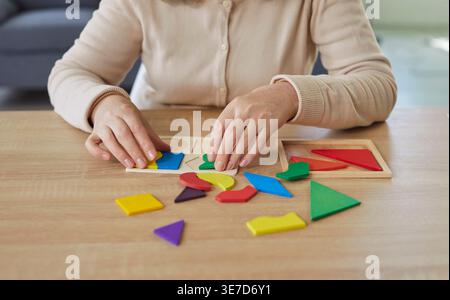 Ritratto ritagliato di una donna anziana che raccoglie figure geometriche in legno a casa seduta al tavolo Foto Stock