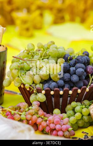 Primo piano di uva verde, rossa e blu scuro in un cestino decorativo in legno servito a un picnic all'aperto o a un festival estivo. Foto Stock