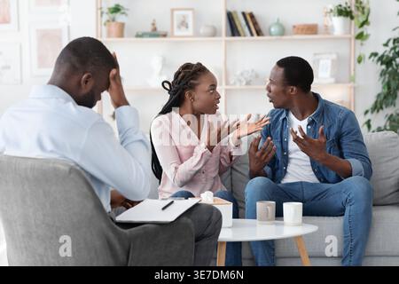 Coppia nera che litiga mentre si siede sul divano e ha una consulenza matrimoniale con un terapista di sesso maschile nero in ufficio Foto Stock