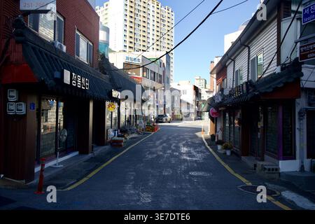 Una strada tranquilla vicino al porto di Bangeojin corre tra bassi negozi e vecchi edifici a Dong-GU, con un'alta torre di appartamenti sullo sfondo. Foto Stock