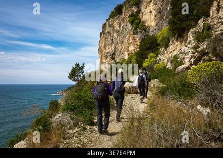 Sperlonga, Italia - 15 marzo 2026: Un gruppo di escursionisti segue uno stretto sentiero roccioso lungo le scogliere calcaree. L'immagine documenta la rete di traccia esterna Foto Stock