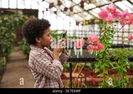 Ragazzo di corsa mista che scatta foto di fiori utilizzando lo smartphone in giardino Foto Stock