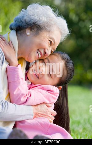 La nonna e la nipote cinesi si abbracciano seduti sul prato del parco durante il giorno Foto Stock