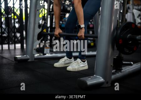 Donna thailandese che indossa abbigliamento fitness e fa deadlift alla macchina smith in palestra Foto Stock