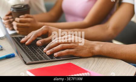 Uomo nero che usa il portatile accanto ai suoi amici a tavola in biblioteca Foto Stock