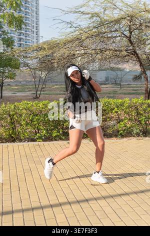 Donna ispanica in abbigliamento sportivo e berretto che pratica tecniche di boxe nel parco nelle giornate di sole Foto Stock