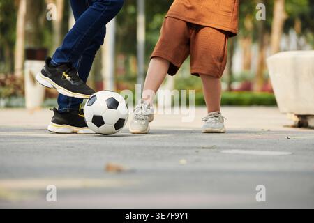 Primo piano del padre asiatico che gioca a calcio con il figlio nel parco Foto Stock