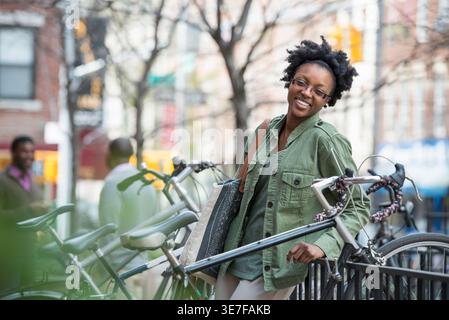 Donna nera appoggiata su ringhiere in piedi vicino alle biciclette in città durante il giorno Foto Stock