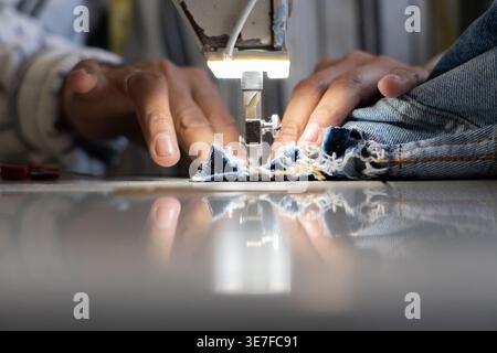 Immagine ritagliata di un sarto ispanico di mezza età che cucita con le mani su una macchina da cucire in un negozio di sartoria Foto Stock