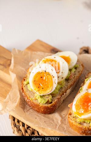 Pane artigianale croccante con guacamole cremoso e uova perfettamente jammy. Questo scatto luminoso ad angolo alto offre un'illuminazione naturale che mette in risalto il Foto Stock