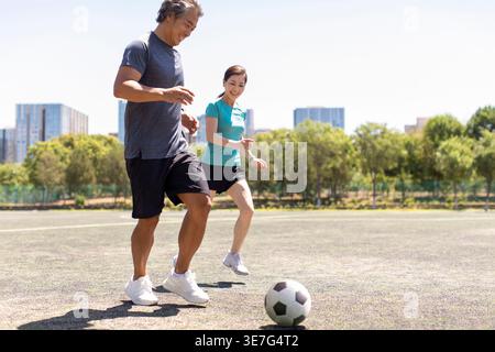 Sorridente coppia cinese di mezza età che gioca a calcio sul campo di calcio nelle giornate di sole Foto Stock