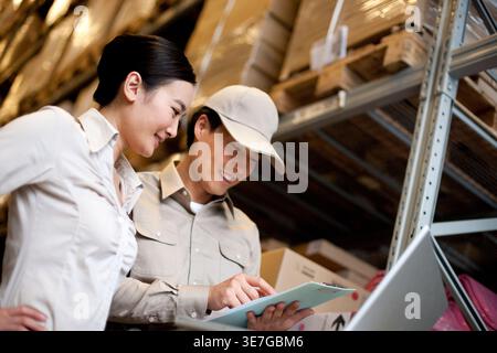 Lavoratore cinese di sesso maschile e femminile che detiene appunti che controlla le scorte in magazzino Foto Stock