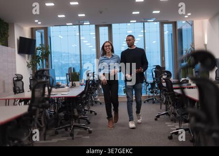 Un uomo nero sorridente e una donna caucasica che parla mentre cammina in ufficio Foto Stock