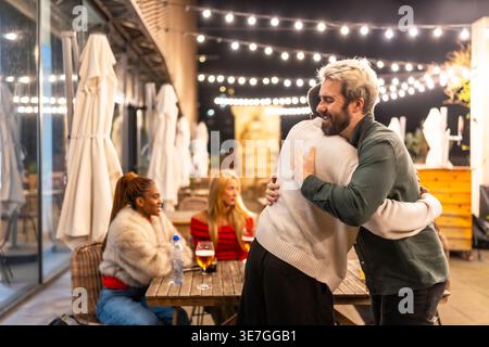 Gruppi di amici diversi che si abbracciano e si salutano mentre arrivano al bar sul tetto di notte Foto Stock