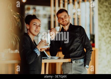 Donna d'affari ispanica sorridente e uomo d'affari caucasico che prende una tazza di caffè in un caffè Foto Stock
