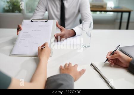 Mano di donna che firma un documento tenuto da un uomo d'affari indiano seduto a un tavolo in ufficio Foto Stock