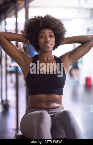 Allegra donna nera con afro che indossa abiti fitness facendo esercizio su una panca ab in palestra Foto Stock