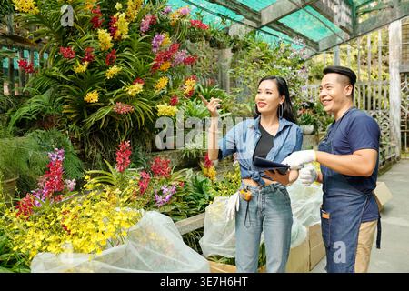 Donna asiatica che parla con un lavoratore maschile che guarda lontano in serra Foto Stock