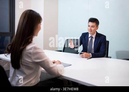 Sorridente candidato cinese seduta a tavola guardando un manager delle risorse umane uomo asiatico che parla durante un colloquio di lavoro in ufficio Foto Stock