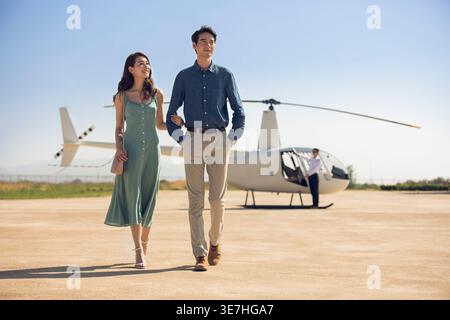 Coppia cinese sorridente che cammina vicino all'elicottero sulla pista Foto Stock
