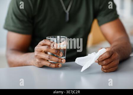 Mani di militari neri che tengono il tessuto e un bicchiere d'acqua seduti a tavola in clinica Foto Stock