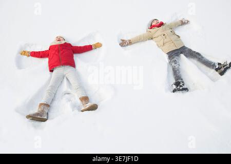 Allegri bambini cinesi che creano angeli di neve mentre sdraiati sulla neve durante l'inverno Foto Stock