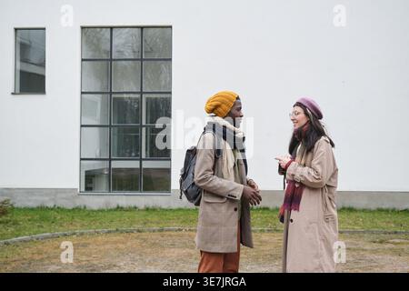 Uomo nero e donna caucasica in abiti caldi che conversano insieme in città Foto Stock