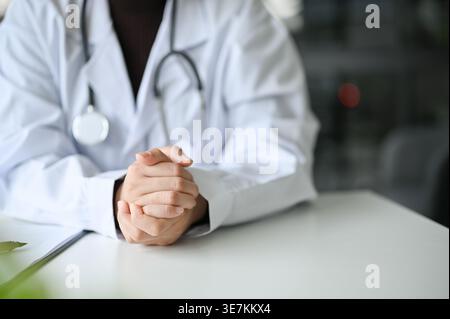 Donna asiatica dottore seduto con le mani schiacciate a tavola in clinica Foto Stock