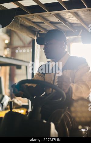 Uomo nero di mezza età che guida un carrello elevatore a forche in magazzino Foto Stock